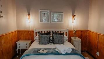 Une chambre avec un plafond en bois, un lit avec une literie blanche, deux tables de chevet et des lampes fixées au mur.