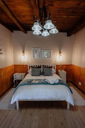Une chambre avec un plafond en bois, un lit avec une literie blanche, deux tables de chevet et des lampes fixées au mur.