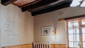 A bedroom with a bed, a dresser, a chair, a bedside table, a wall-mounted lamp, and a window. - Dassenheuwel Farm Stay Homestead (Malmesbury)