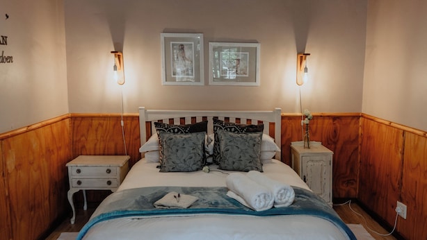 A bedroom with a wooden ceiling, a bed with white bedding, two bedside tables with lamps, and two framed pictures on the wall. - Dassenheuwel Farm Stay Homestead (Malmesbury)