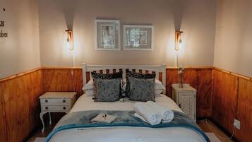 Une chambre avec un plafond en bois, un lit recouvert de linge de lit blanc, deux tables de chevet avec des lampes et deux tableaux encadrés accrochés au mur.