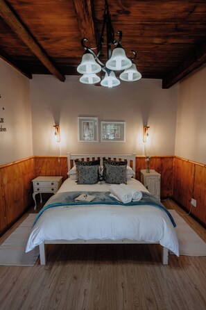 Un dormitorio con techo de madera, una cama con ropa blanca, dos mesitas de noche con lámparas y dos cuadros enmarcados en la pared.