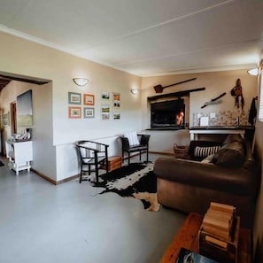 Una sala de estar con chimenea, un sofá, una zona de comedor y una pared decorada con cuadros.
