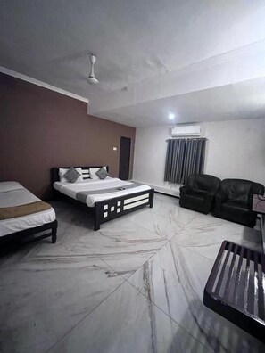 Quarto de hotel com cama, sofá, mesa de centro e ventoinha no teto.