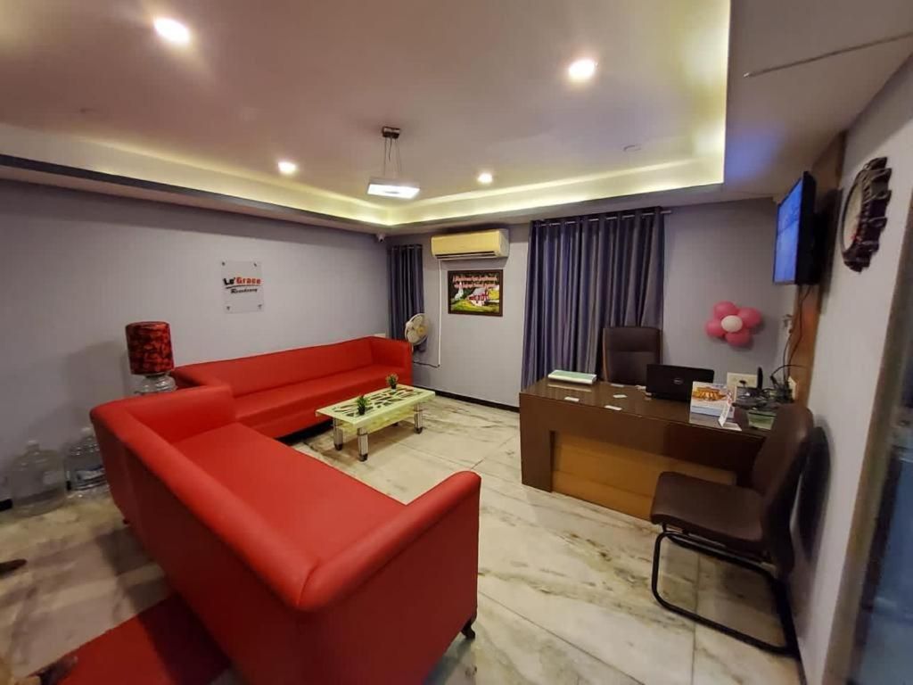 Un área de recepción con un sofá rojo, una mesa de centro de madera, un mostrador de recepción y un televisor montado en la pared.