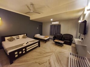 Quarto de hotel com cama, sofá, mesa de centro, televisão e ar condicionado.