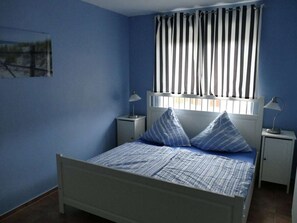 A bedroom with a single bed, two bedside tables, and a window with vertical blinds. - Maritime House Semi-detached House Wismar (Klütz)