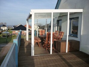 A covered outdoor seating area with a table and chairs, a wooden deck, and a view of the neighborhood. - Maritime House Semi-detached House Wismar (Klütz)