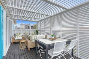 Ein überdachter Außenbereich mit Tisch und Stühlen, einer Rattan-Couch und Blick ins Freie.