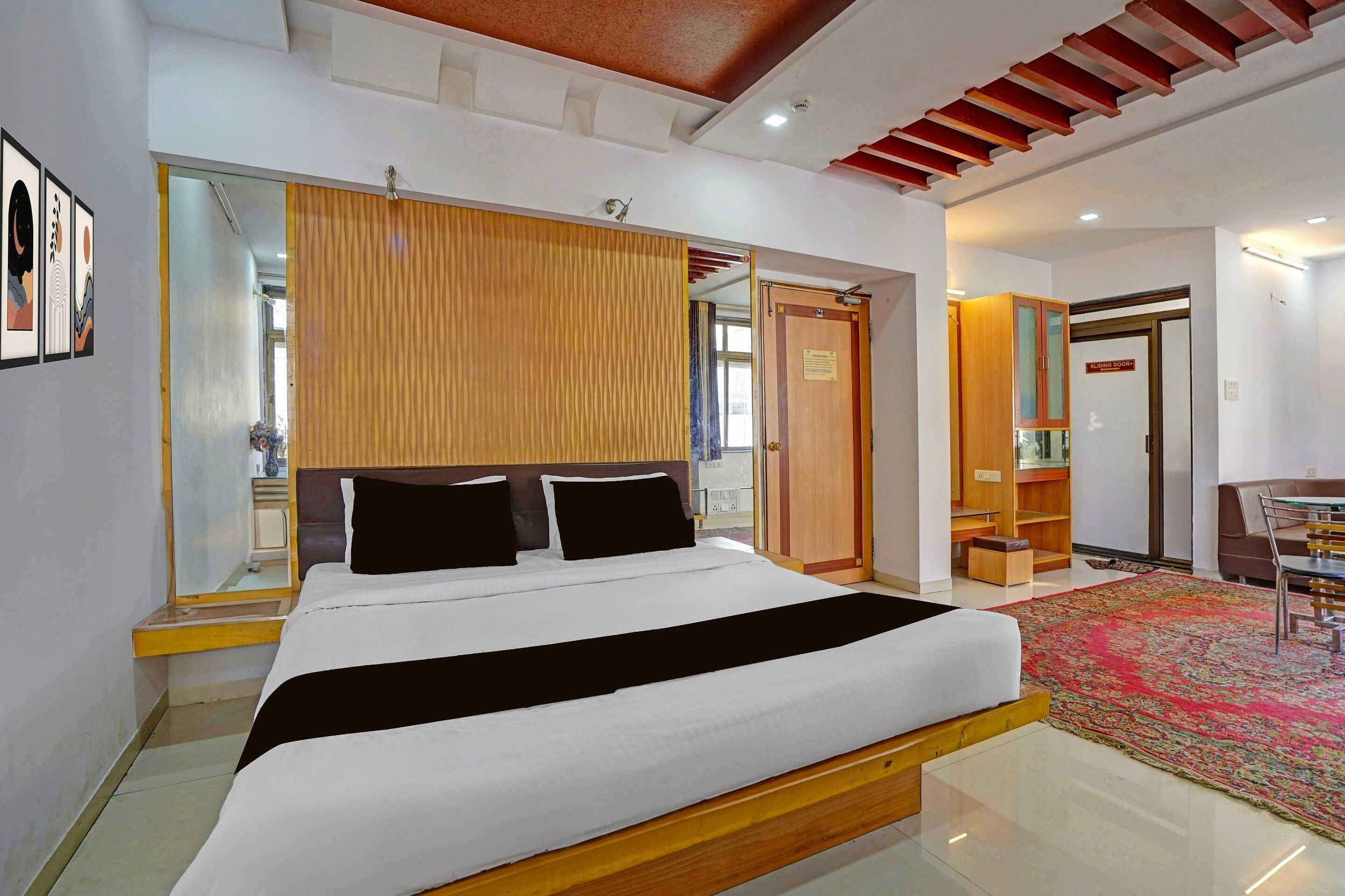 A modern bedroom with a bed, a wooden headboard, a mirror, a sliding door, and a small seating area with a chair and table.