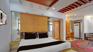 Un dormitorio moderno con cama, cabecero de madera, espejo, puerta corrediza y una pequeña zona de estar con una silla y una mesa.