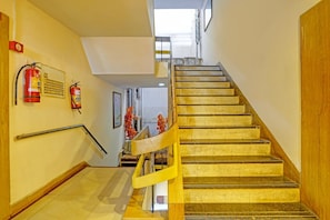 A staircase with a wooden handrail and a fire extinguisher mounted on the wall. - Classic Hotel Vrundavan Residency (Vadodara)