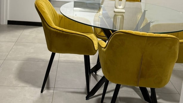 A modern kitchen with white cabinets, a stove, and a kettle. There is a glass table with two yellow chairs. - Apartment in Stay Near Montecasino (Johannesburg)