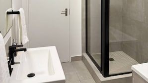 A modern bathroom with a white sink, a glass shower enclosure, and a door. - Apartment in Stay Near Montecasino (Johannesburg)