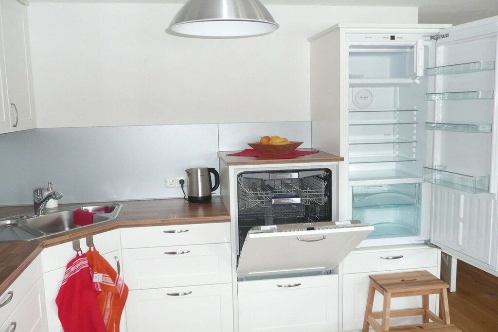 A kitchen with a built-in dishwasher, a sink, and a wooden stool.