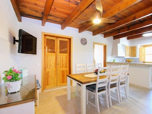 A dining area with a wooden table and chairs, a ceiling fan, and a kitchen area with wooden cabinets and a window. - Cabin in Muro With Swimming Pool (Muro)