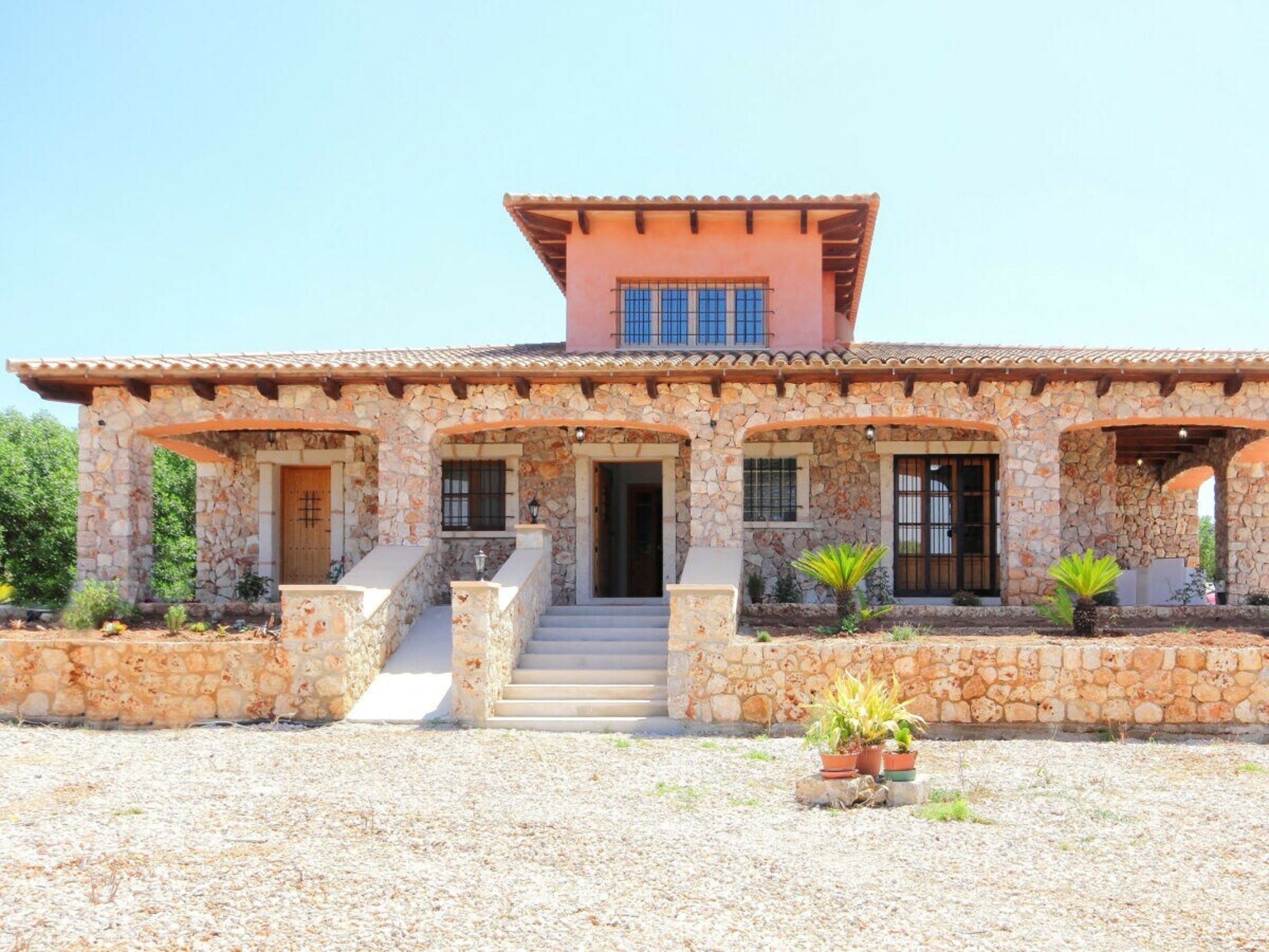 A stone house with a tiled roof, a central staircase, and potted plants.