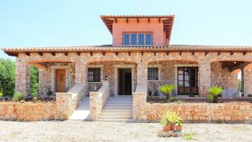 A stone house with a tiled roof, a central staircase, and potted plants.