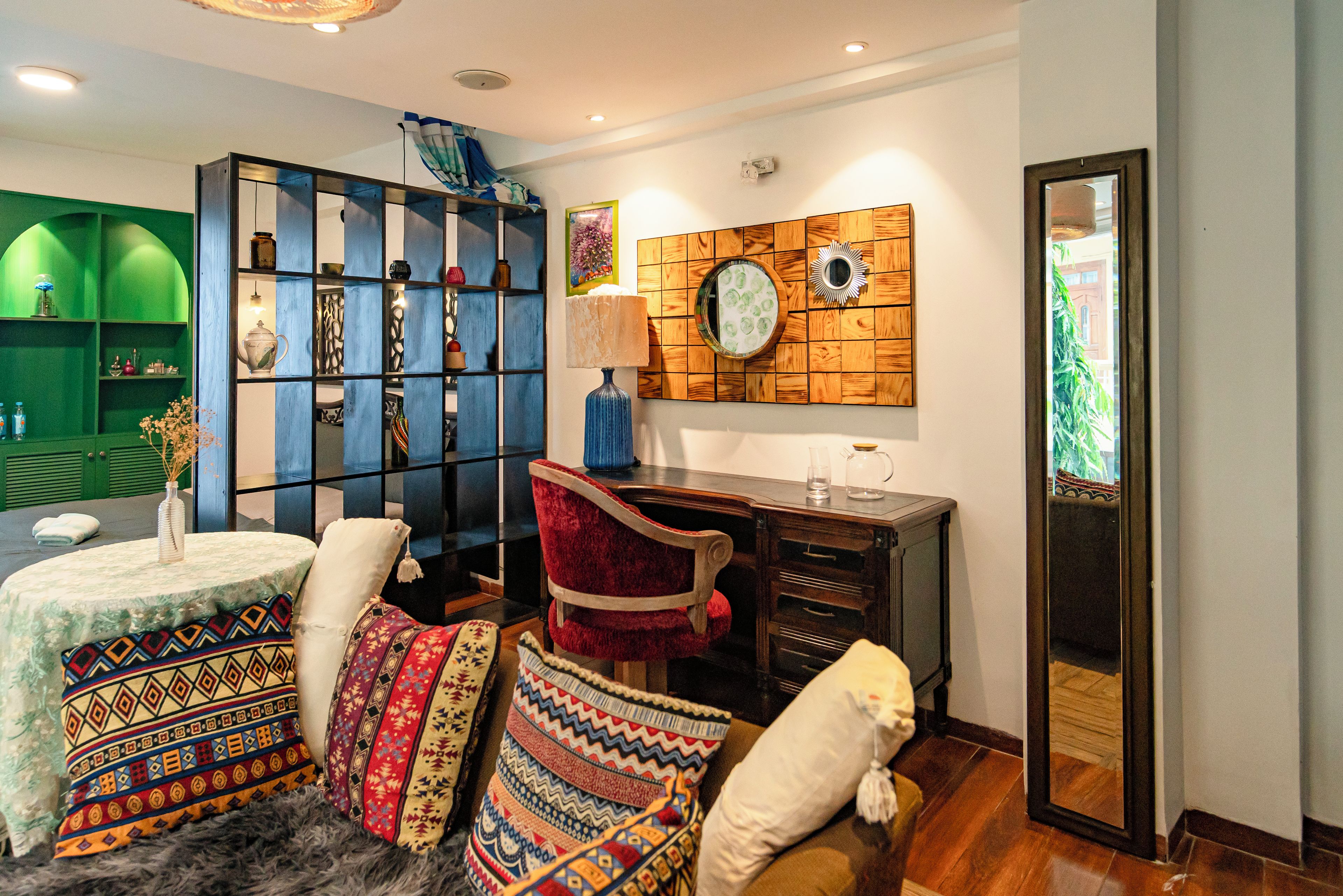 A room with a green shelving unit, a red chair, a patterned sofa, and a wooden wall decor.