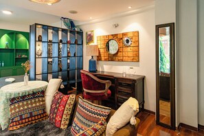Ein Zimmer mit einer grünen Regaleinheit, einem roten Sessel, einem gemusterten Sofa und einer Holzdeko an der Wand.