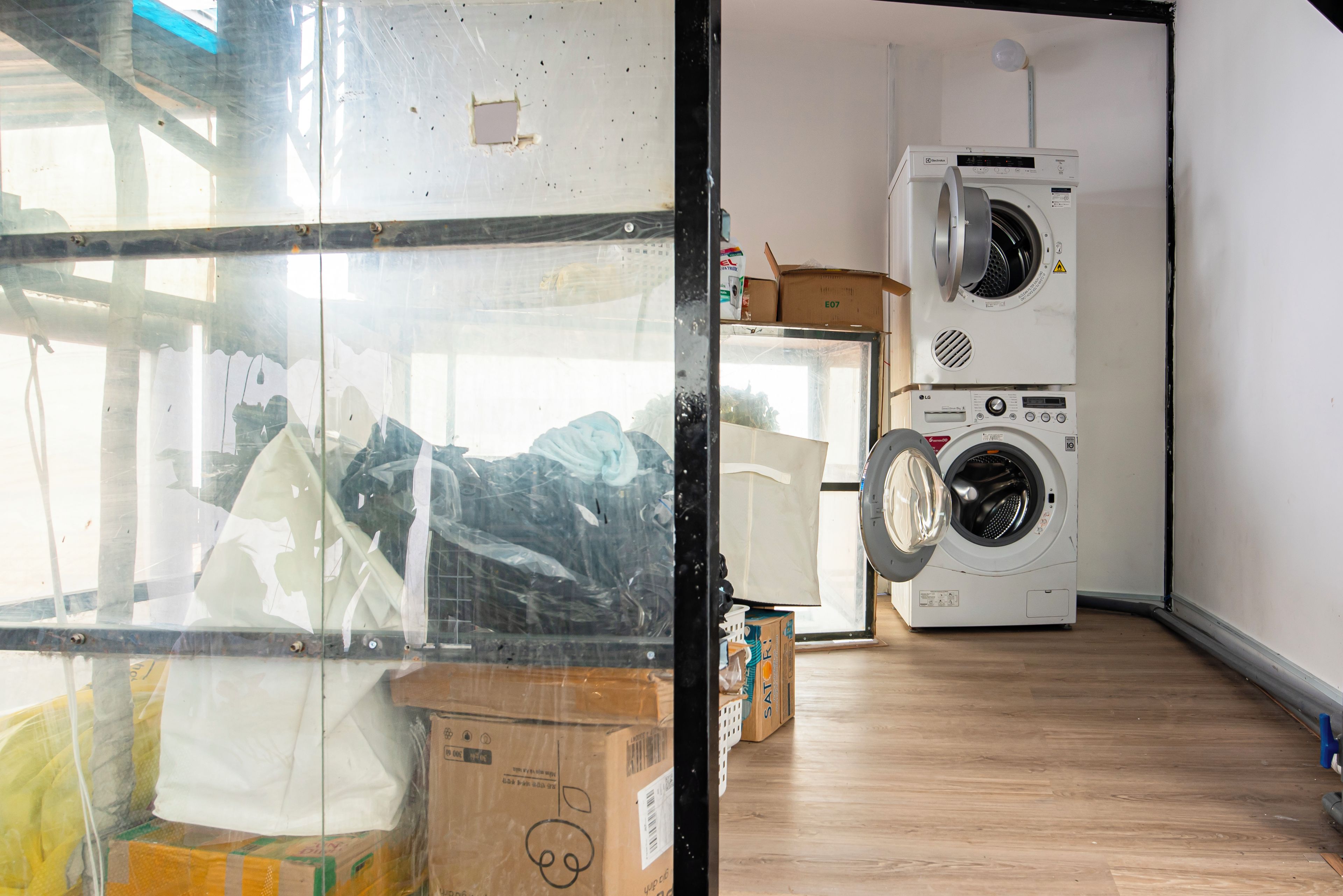 A room with a large window, a washing machine, and stacked cardboard boxes.