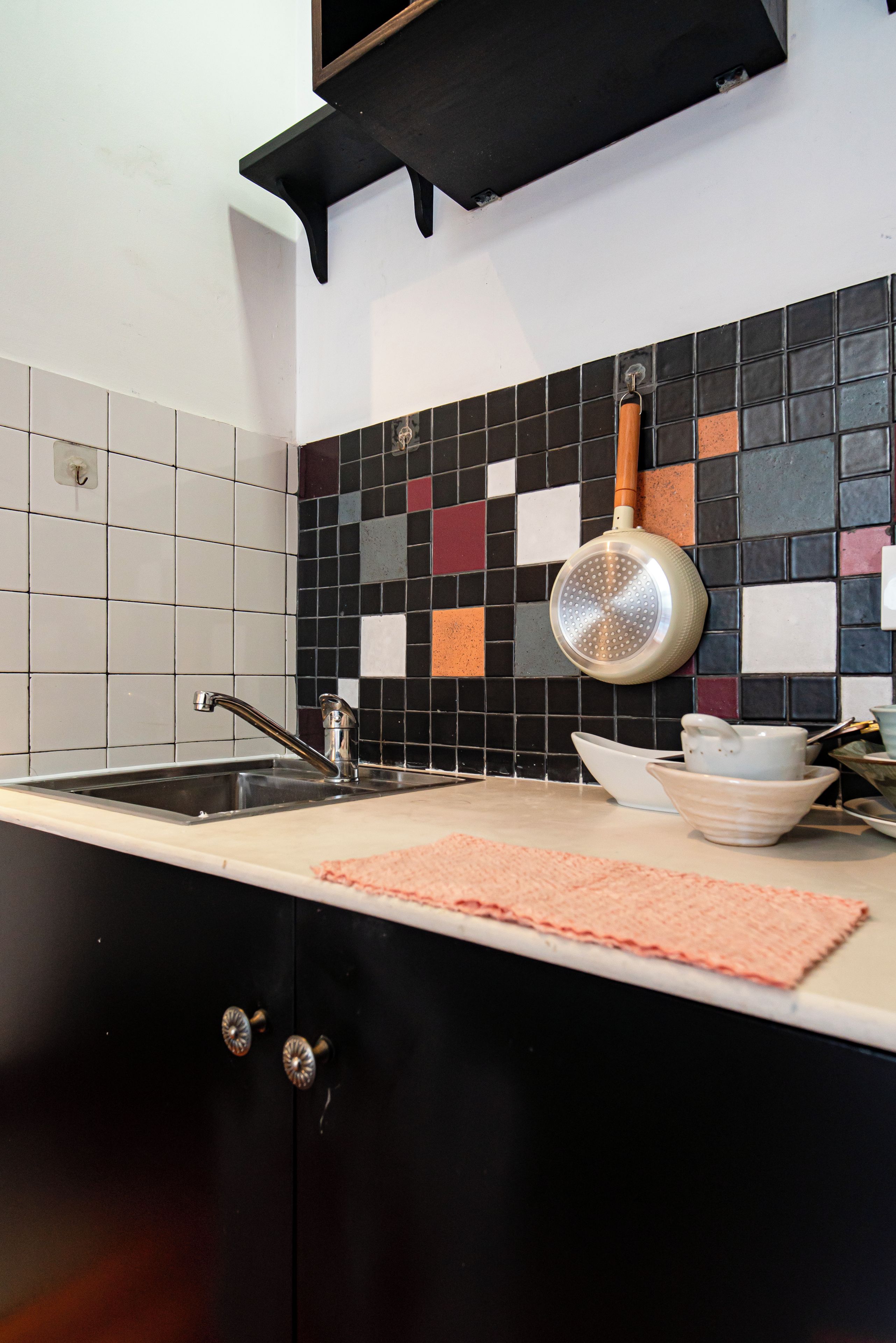 Eine Küche mit schwarz-weißer Wandfliesen, einem Edelstahl-Spülbecken und einem an der Decke befestigten Topfregal.