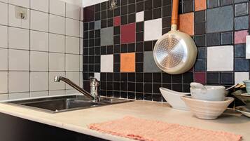 Eine Küche mit schwarz-weißer Wandfliesen, einem Edelstahl-Spülbecken und einem an der Decke befestigten Topfregal.