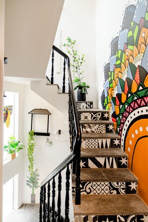 Una escalera con peldaños estampados y barandilla negra, que conduce a una habitación con un mural colorido.