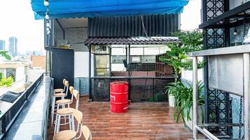 Una terraza en la azotea con sillas y mesas de madera, un barril rojo y plantas en macetas.