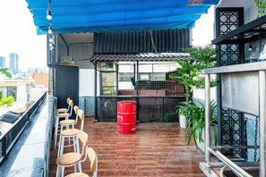 Eine Dachterrasse mit Holzkubeln und Tischen, einem roten Fass und Topfpflanzen.
