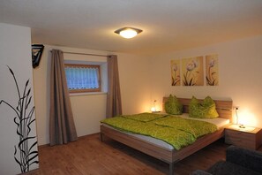 Une chambre à coucher avec un lit en bois, une literie verte, une fenêtre avec des rideaux et des œuvres d’art murales.