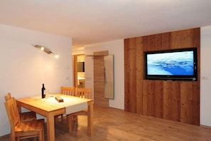 A dining area with a wooden table and chairs, a television mounted on a wooden wall, and a wooden floor. - L-XL up to 12 people (ahrntal)