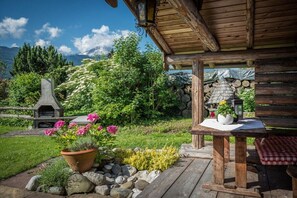 Um deck de madeira com mesa e banco, rodeado por um jardim com flores e um muro de pedra.
