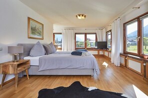 Een slaapkamer met een bed, een televisie, een raam met gordijnen en een schilderij aan de muur.