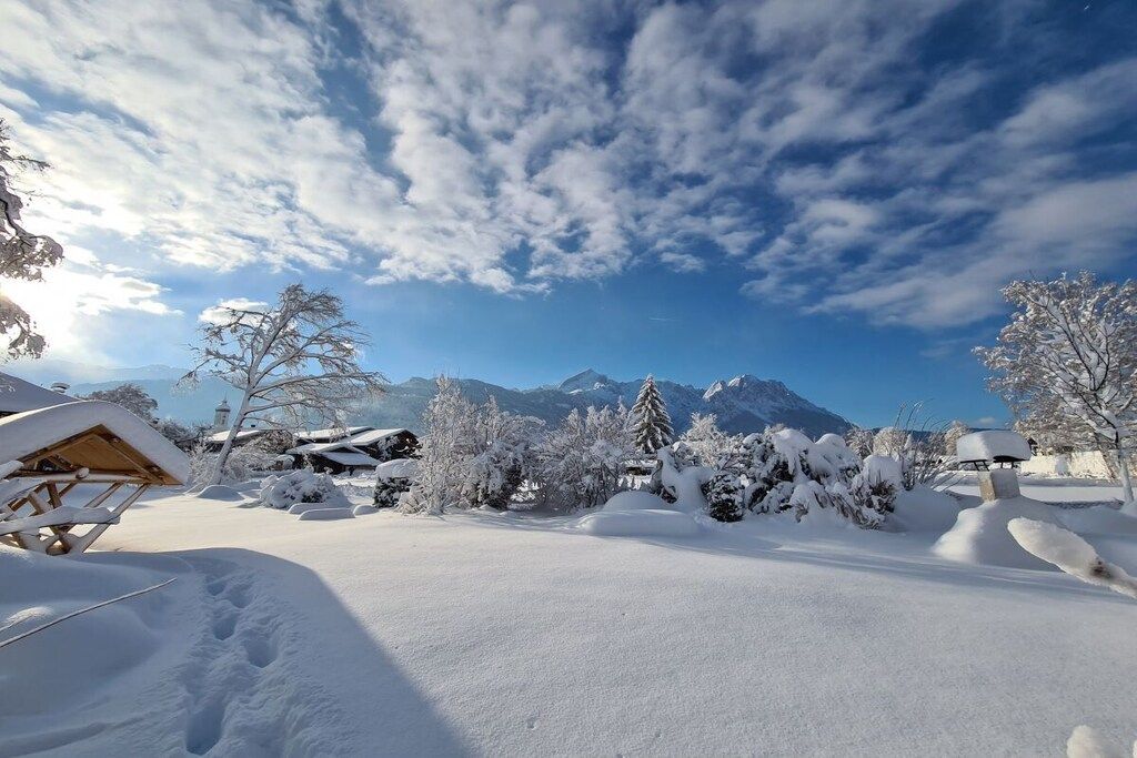 Eine verschneite Landschaft mit einer Holzhütte, schneebedeckten Bäumen und Bergen im Hintergrund.