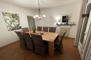 A dining area with a wooden table and wicker chairs, a chandelier, and a wall-mounted shelf with decorative items. - Holiday home in Flayosc with swimming pool (Flayosc)