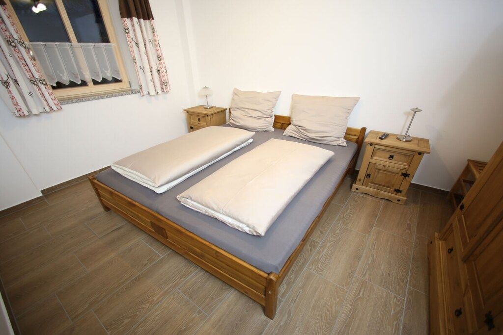 A bedroom with a wooden bed, two bedside tables, a nightstand, and a window with curtains.