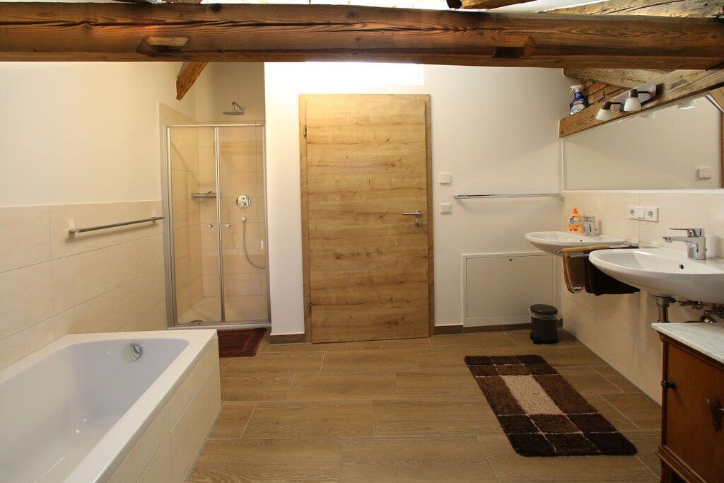 Une salle de bain avec une baignoire, une douche, une porte en bois, un lavabo et un miroir.