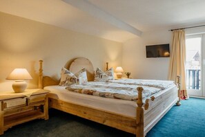 Een tweepersoonsbed met houten frame, twee nachtkastjes met lampen, een grote ronde spiegel boven het bed en een televisie aan de muur.