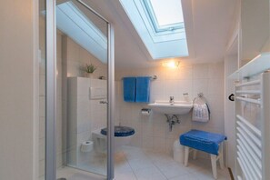 Een kleine badkamer met dakraam, douchecabine, toilet en wastafel.