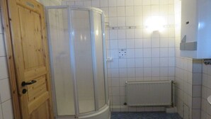 Een badkamer met een houten deur, een glazen douchecabine, witte betegelde wanden en een witte radiator.