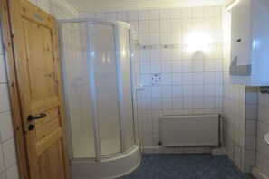 Et badeværelse med en trædør, glasbrusekabine, hvidmalede vægge og en hvid radiator.