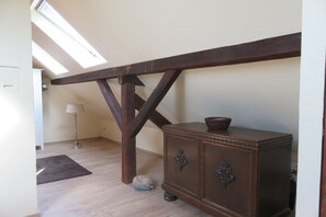 A room with a sloped ceiling, a wooden beam structure, a cabinet with two drawers, a small rug, and a floor lamp.