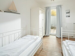 A bedroom with two single beds, a window with curtains, a radiator, and a small sailboat decoration. - Holiday Apartment With 2 Bedrooms (Norderney)