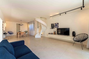 A modern living room with a blue sofa, a TV, and a spiral staircase. - Solemar Sicilia - Villa Mondello (Palermo)