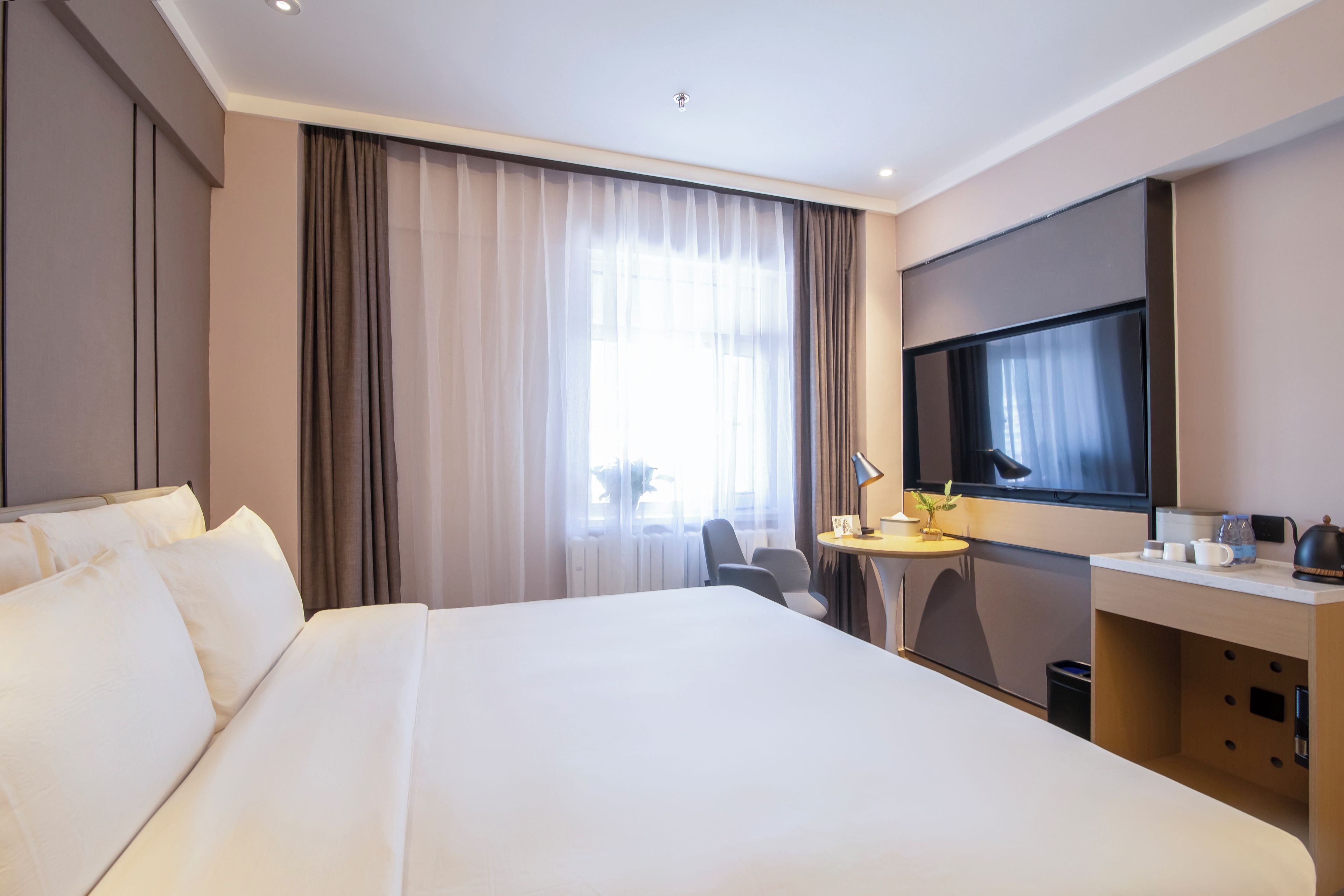 Habitación de hotel con una cama grande, un escritorio con silla, un televisor montado en la pared y una ventana con cortinas.