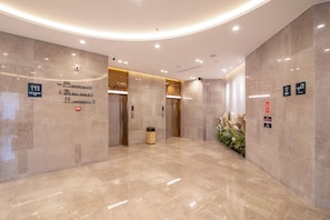 Eine moderne Lobby mit Marmorboden, einer Rezeption und Hinweisschildern zu Einrichtungen wie einem Restaurant, einer Toilette und einem Aufzug.
