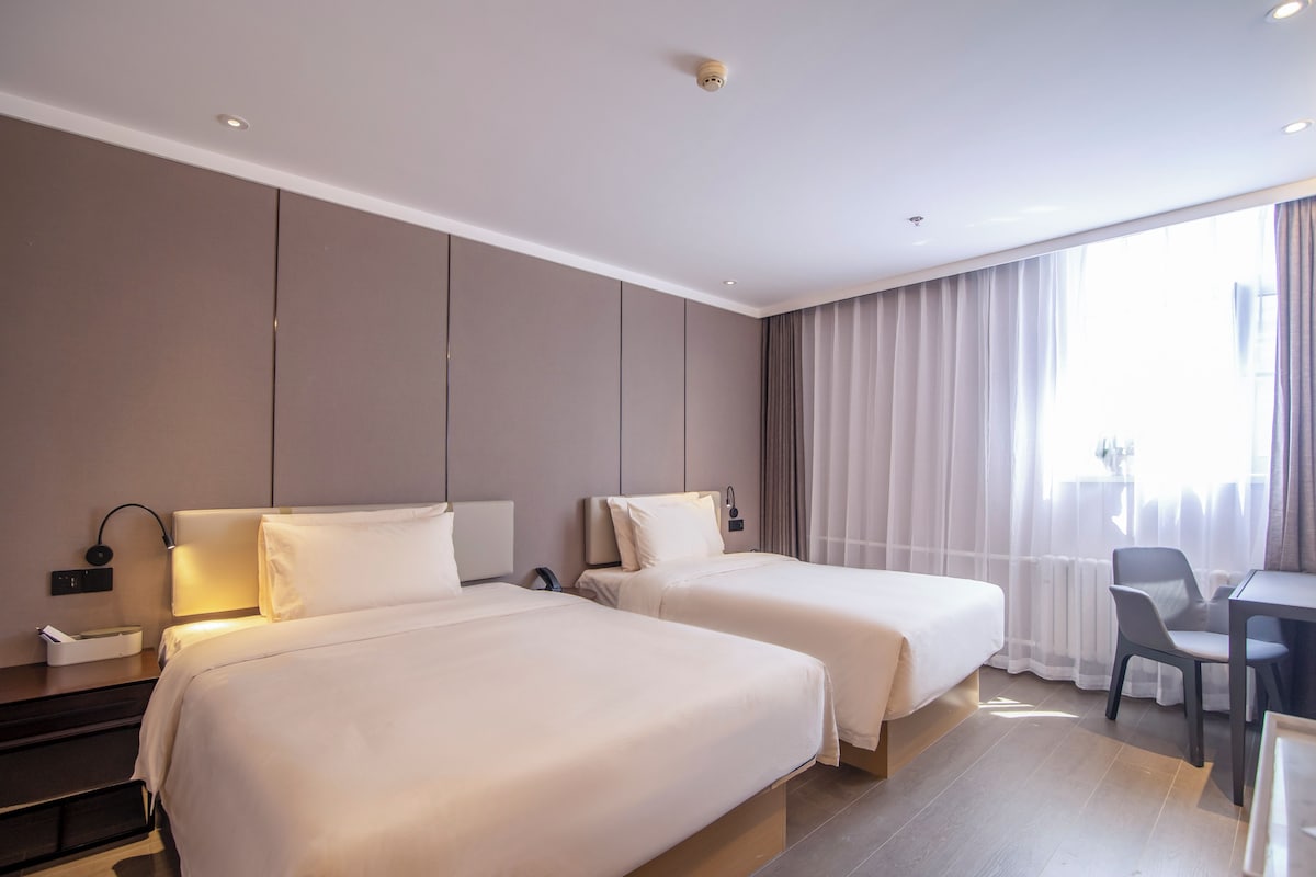 Ein Hotelzimmer mit zwei Betten, einem Schreibtisch, einem Stuhl und einem Fenster mit Vorhängen.