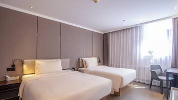 Ein Hotelzimmer mit zwei Betten, einem Schreibtisch, einem Stuhl und einem Fenster mit Vorhängen.
