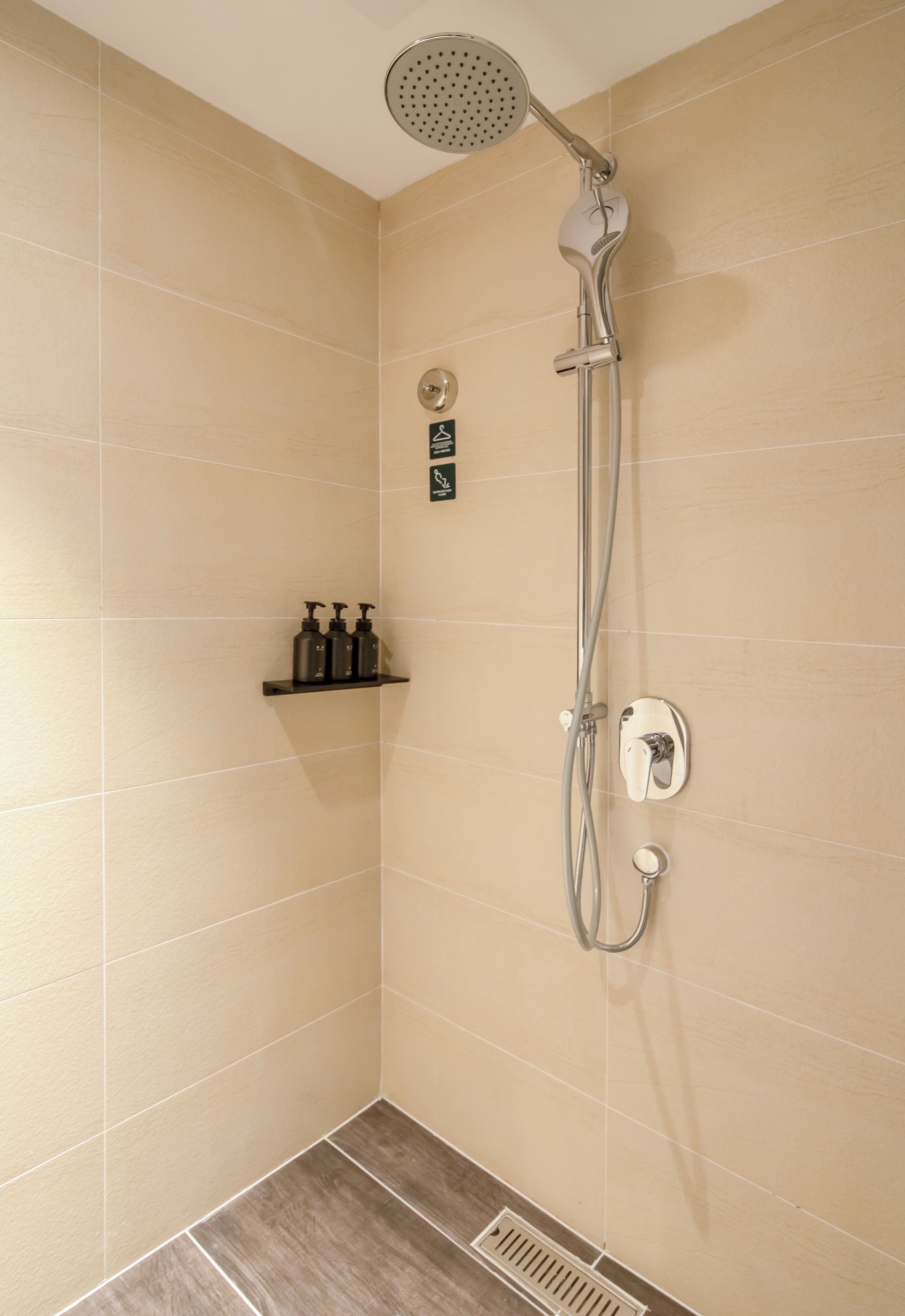 A shower with a handheld showerhead, a wall-mounted control, and a shelf with toiletries.